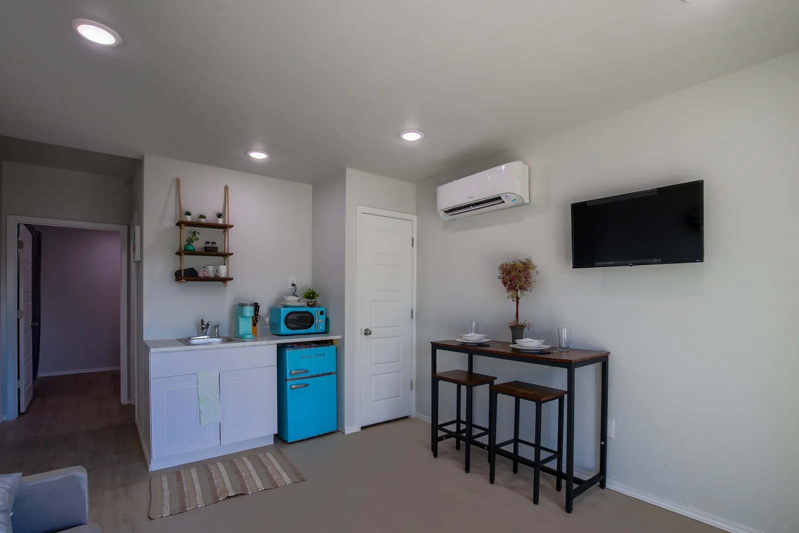 Furnished container-home interior with kitchenette, dining set, and wall-mounted TV in Canyon Lake, Texas
